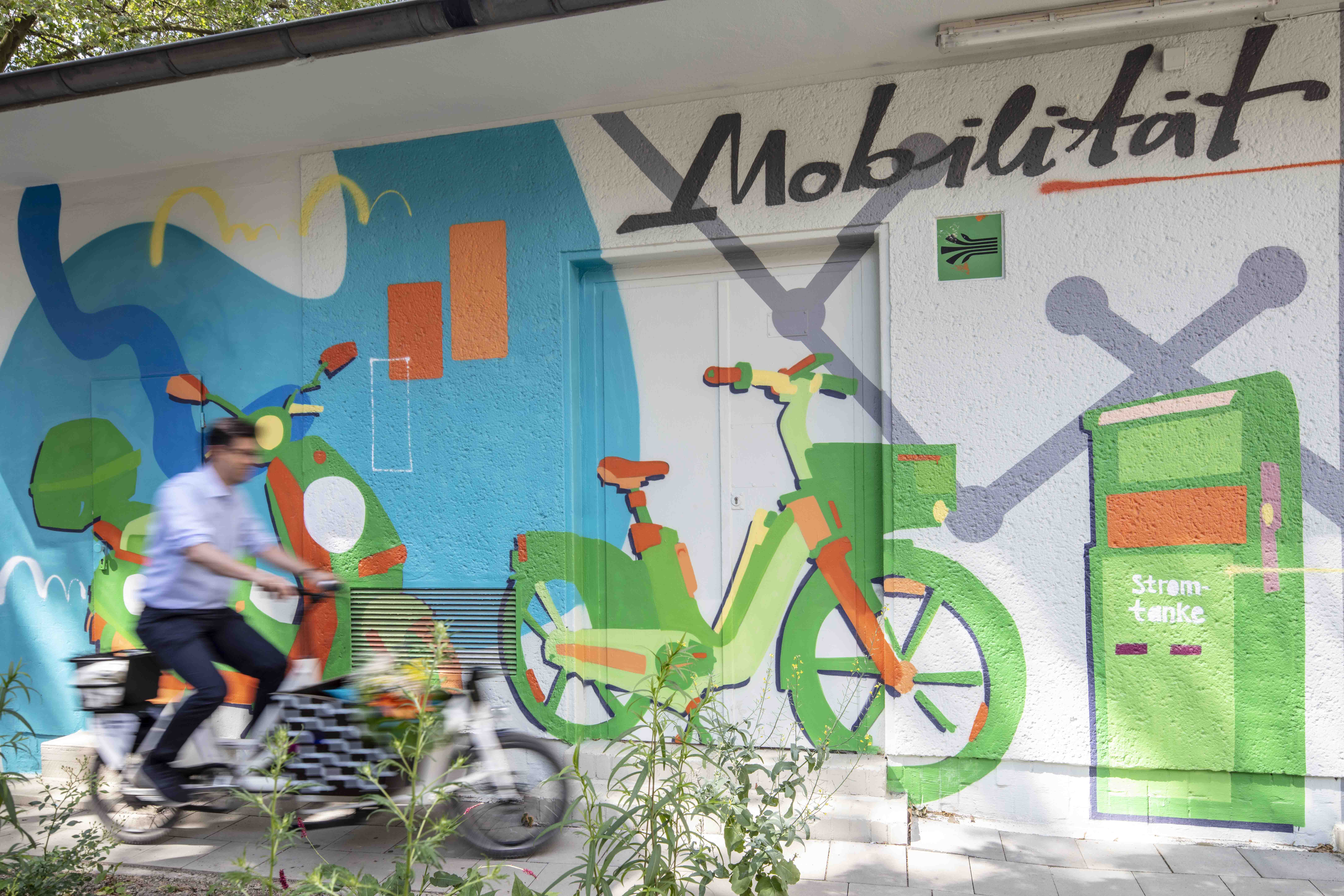Eine Person fährt mit einem Lastenfahrrad vor einem Graffiti